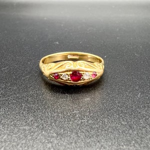 May include: A gold ring with a red ruby and white diamonds set in a decorative band.
