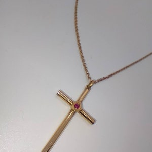 May include: A gold chain necklace with a gold cross pendant featuring a red gemstone in the centre.