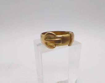 May include: A gold-coloured ring with a buckle design.