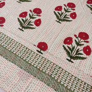 May include: Cream-coloured textile featuring a repeating pattern of red floral bouquets and green leaves. The fabric is stitched with red and green threads, and the border has a green and white striped design. Suitable for bedding or home decor.