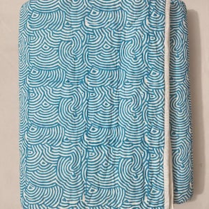 May include: A folded, rectangular quilt with a repeating pattern of teal blue and white concentric wave-like shapes. The quilt has a white border along one edge.