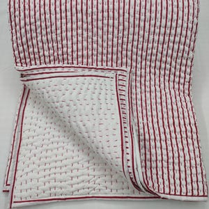 Puede incluir: Edredón a rayas blancas y rojas con una esquina doblada, que revela las costuras interiores. El edredón presenta rayas rojas verticales sobre un fondo blanco, con un borde rojo. Las costuras son visibles.