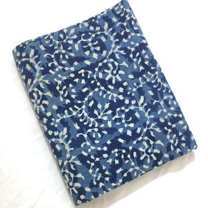 May include: Folded fabric with a blue and white floral pattern. The fabric has a dark blue background with a repeating design of white floral shapes. The fabric is folded neatly, showing the pattern clearly.