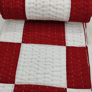 Red and white patchwork Kantha quilt on bed.