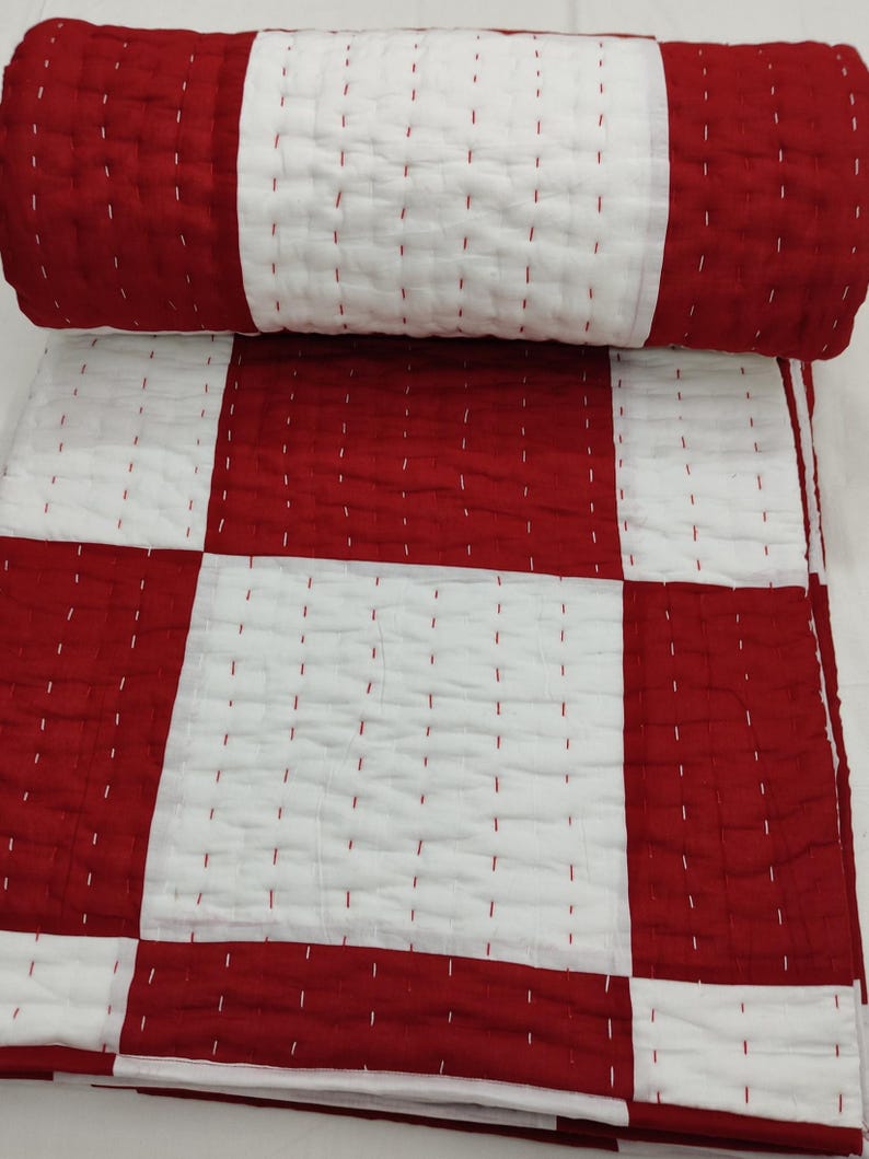 Red and white patchwork Kantha quilt on bed.