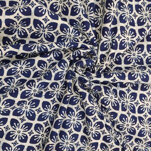 Peut inclure: Gros plan sur un tissu avec un motif floral répétitif. Le motif présente des fleurs bleu marine sur un fond crème. Le tissu est froissé, montrant la texture et les plis du matériau.