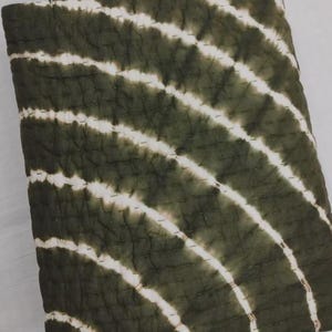 May include: A folded, olive green quilt with white, diagonal stripes. The quilt has a stitched pattern throughout. The fabric appears to be soft and textured. The overall design is simple and modern.