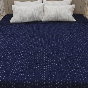 Peut inclure: Un couvre-lit bleu marine à motifs pointillés et quatre oreillers blancs sur une tête de lit en bois. Les oreillers ont un aspect texturé et matelassé. Le couvre-lit est bien rangé, suggérant une mise en avant de la literie et de la décoration intérieure.