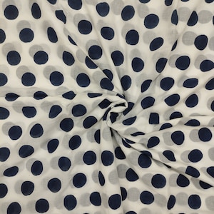 May include: White fabric with a repeating pattern of large, navy blue polka dots. The fabric is gathered and folded, creating shadows and depth. The polka dots are evenly spaced and vary slightly in size.