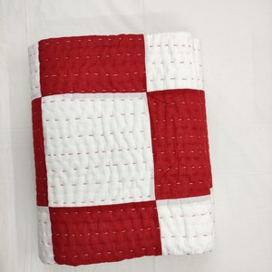 Close-up of hand-stitched red and white cotton quilt pattern.