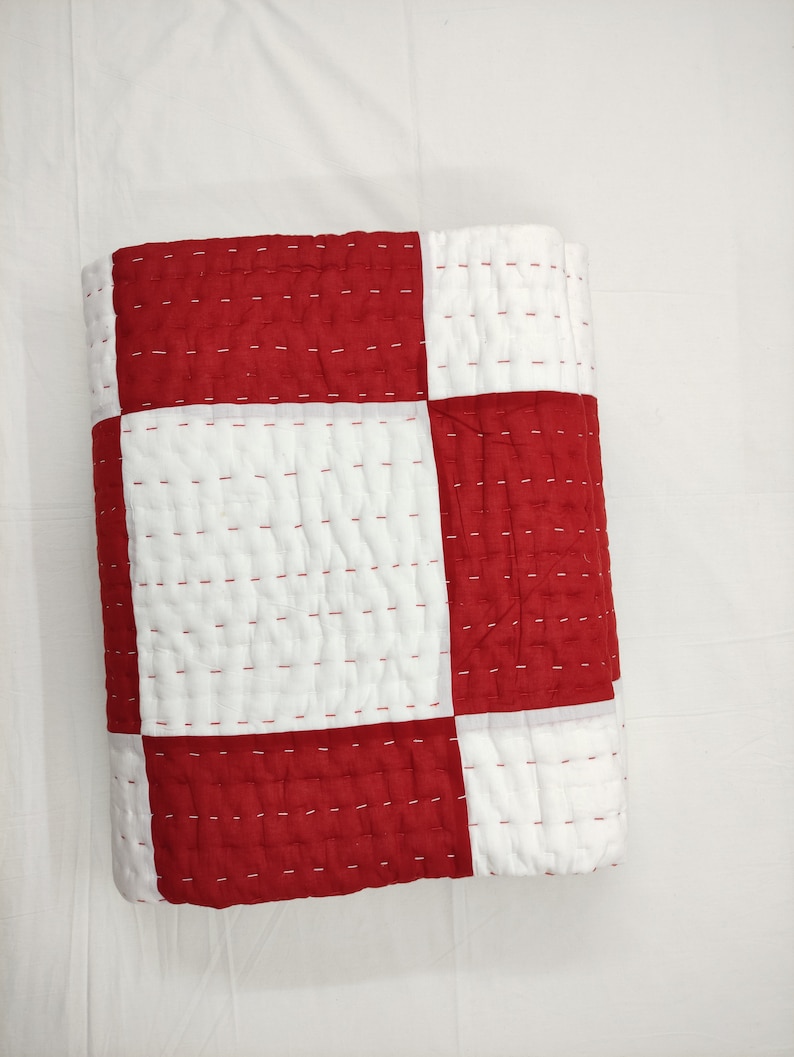 Close-up of hand-stitched red and white cotton quilt pattern.