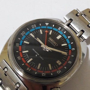 May include: A black Seiko automatic watch with a silver band. The watch face has a black background with white markings and a red and blue bezel. The watch face also has the text "SEIKO AUTOMATIC" and "NAVIGATOR TIMER".