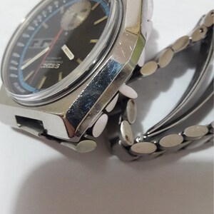 May include: A silver wristwatch with a black face and a silver metal band. The watch has a chronograph function and a date window.