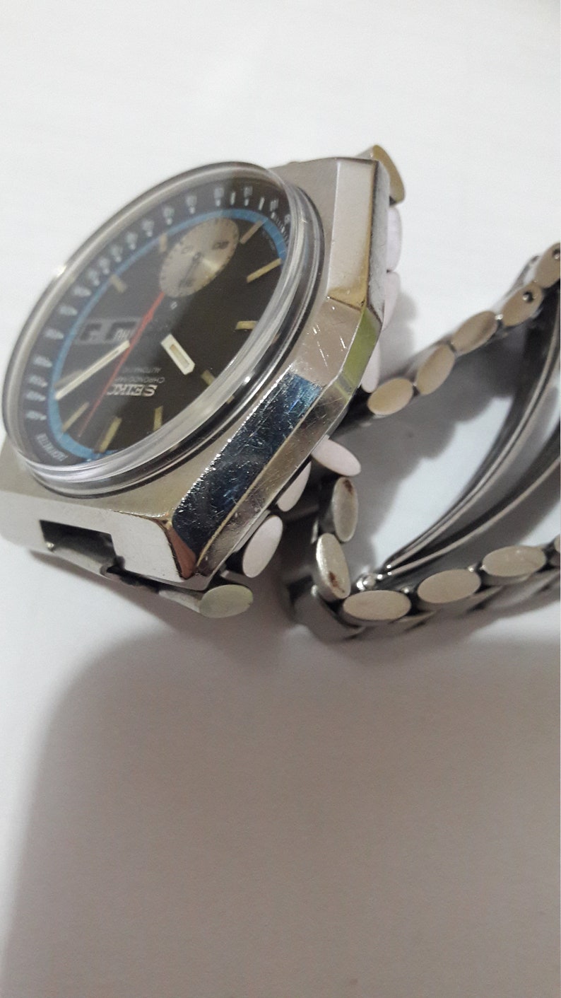 May include: A silver wristwatch with a black face and a silver metal band. The watch has a chronograph function and a date window.
