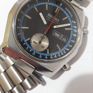 May include: A silver Seiko chronograph wristwatch with a black face, blue and white markings, and a red second hand. The watch has a silver metal band and a date window that displays "THU 4".