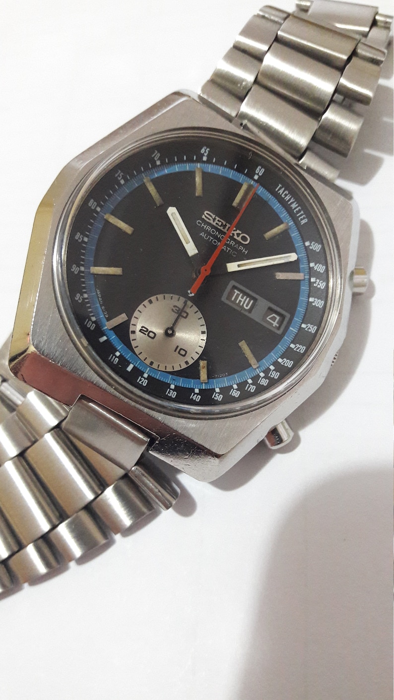 May include: A silver Seiko chronograph wristwatch with a black face, blue and white markings, and a red second hand. The watch has a silver metal band and a date window that displays "THU 4".