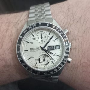 May include: A silver Citizen chronograph wristwatch with a white face and black markings. The watch has a tachymeter scale and a date window that displays "THU 2".