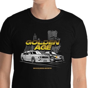 Puede incluir: Camiseta negra con un gráfico amarillo y blanco de dos coches clásicos y las palabras "GOLDEN AGE". La camiseta también incluye el texto "BMW M3 E30/MERCEDES-BENZ 190E 2.3-16".