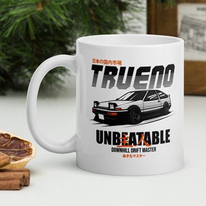 May include: White ceramic mug with a black and white illustration of a car with the text "TRUENO" in orange and "UNBEATABLE" in black. The text "DOWNHILL DRIFT MASTER" is in black and the text "あたるマスター" is in Japanese.