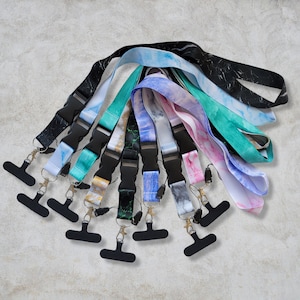 May include: A collection of ten colourful patterned lanyard straps with black metal clasps. The lanyards are made of a soft, flexible material and feature a variety of marble-like patterns.