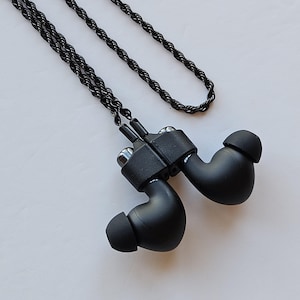 May include: Black in-ear headphones with a black braided cord. The headphones are connected by a black cord and have a black rubber earpiece.