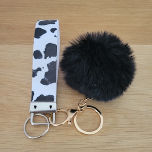 Llavero de pulsera de piel sintética con llavero Pom Pom, cordón de muñeca, llavero con patrón blanco y negro, correa para la muñeca, pulsera con patrón de estampado de vaca