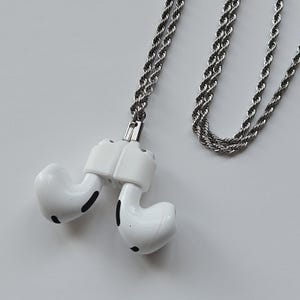 May include: A white AirPod case with a silver chain necklace. The case is attached to the chain with a silver clip.