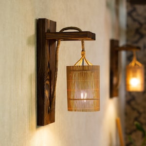 May include: Two wooden wall sconces with woven bamboo shades, each with a warm white light bulb. The sconces are mounted on a beige wall with a white electrical outlet.