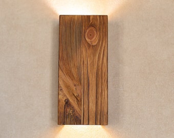 May include: A rectangular wooden wall sconce with a warm light emanating from the bottom. The sconce has a rustic, natural wood finish with visible grain patterns.