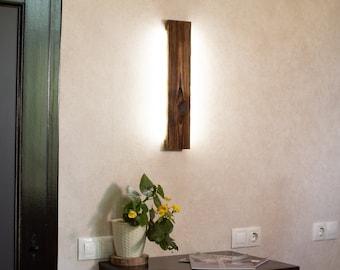 May include: A dark wood wall sconce with a white light fixture, a small potted plant with yellow flowers, and a dark wood dresser with two drawers.