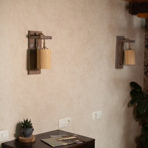 Puede incluir: Dos apliques de pared de madera con pantallas tejidas cuelgan de una pared beige. Una pequeña planta suculenta se encuentra sobre una cómoda de madera oscura con una revista encima.