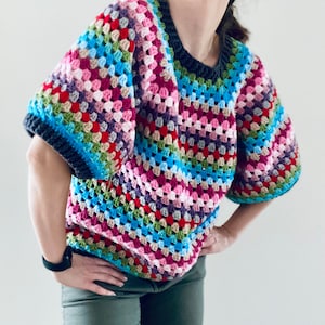 Könnte beinhalten: Ein farbenfrohes Häkeltop mit kurzen Ärmeln und einem gestreiften Muster in den Farben Rosa, Blau, Grün, Rot und Lila.
