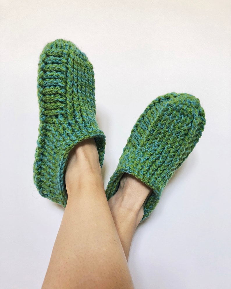 May include: A pair of green and blue crocheted slippers. The slippers are made with a thick yarn and have a simple design.