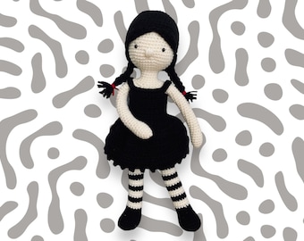 May include: A crocheted doll with black hair, a black dress, and white and black striped stockings. The doll is standing on a white background with a grey pattern.