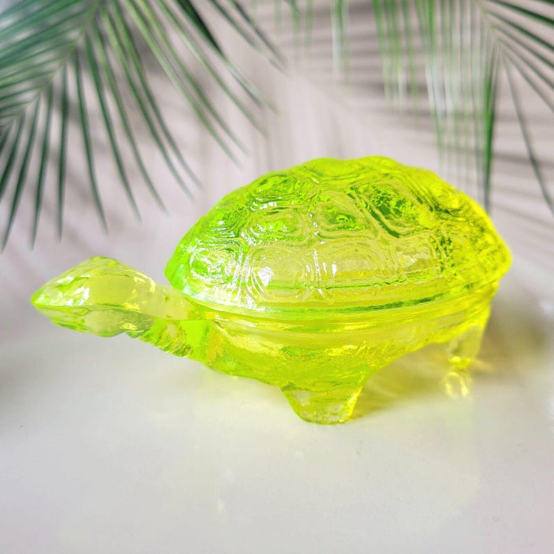 May include: A bright yellow glass turtle trinket box with a detailed shell design. The box is closed and has a smooth, glossy finish.
