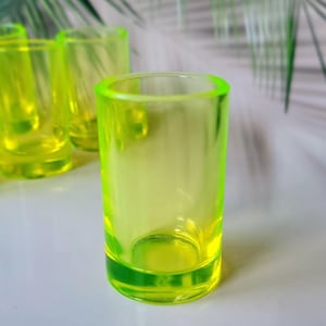 May include: Set of four neon green shot glasses. The glasses are made of glass and have a clear, transparent body. They are perfect for serving shots of spirits or other beverages.