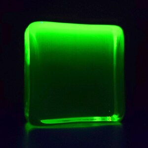 Puede incluir: Un objeto cuadrado brillante con esquinas redondeadas, que emite una luz verde vibrante. El objeto parece estar hecho de un material transl&uacute;cido, con un fondo oscuro.