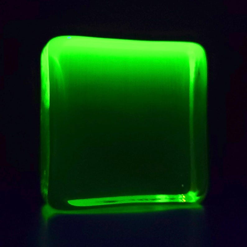 Puede incluir: Un objeto cuadrado brillante con esquinas redondeadas, que emite una luz verde vibrante. El objeto parece estar hecho de un material transl&uacute;cido, con un fondo oscuro.