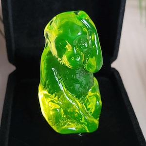 May include: A translucent, green dog figurine. The dog is in a sitting position with its ears drooping. The figurine is made of a glossy material and is set against a black background.