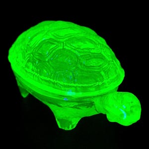 May include: A bright green glass turtle trinket box with a detailed shell design. The box is made of uranium glass and glows under a black light.