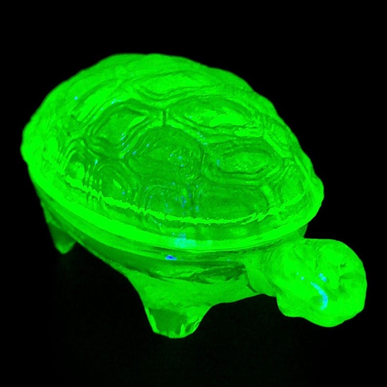 May include: A bright green glass turtle trinket box with a detailed shell design. The box is made of uranium glass and glows under a black light.