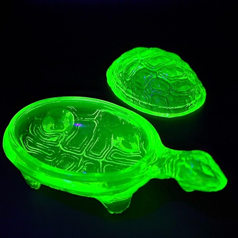 May include: A vintage green glass turtle trinket dish with a matching lid. The dish is made of uranium glass and glows under a black light.