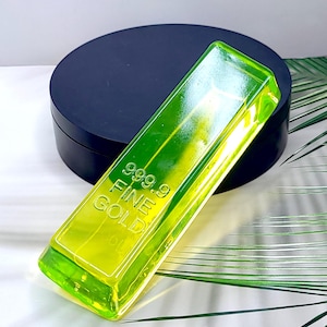 以下が含まれることがあります： 表面に999.9 FINE GOLDの文字が浮き彫りにされた、ネオンイエローの半透明な金塊型バー。滑らかで光沢のある仕上げが施されており、長方形の形状で、光を反射する面取りされたエッジが特徴です。