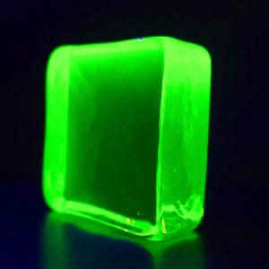Puede incluir: Un objeto rectangular verde ne&oacute;n brillante con esquinas redondeadas. El objeto est&aacute; iluminado, creando una apariencia brillante y vibrante sobre un fondo oscuro. Los bordes del objeto est&aacute;n ligeramente borrosos.