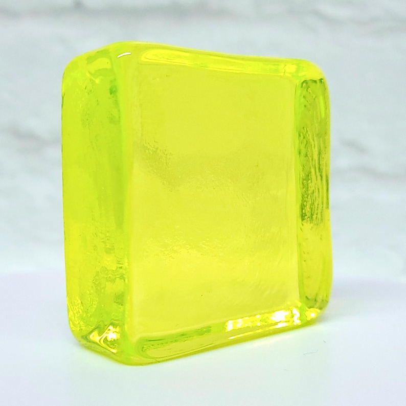 Puede incluir: Un bloque de vidrio amarillo ne&oacute;n transl&uacute;cido con bordes redondeados. El bloque rectangular tiene una superficie lisa y brillante. El vidrio parece s&oacute;lido y de color uniforme, con una ligera textura visible en los lados. Mide unos 5 cm de alto.