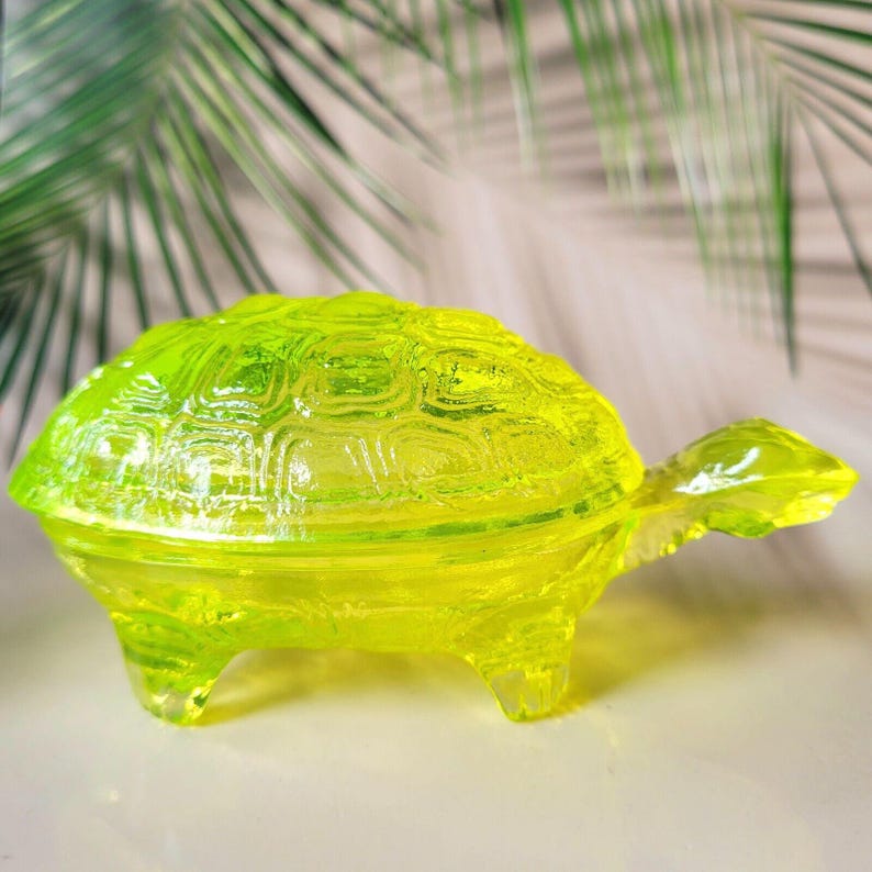 May include: A bright yellow glass turtle trinket box with a detailed shell design. The box is open and has a lid.