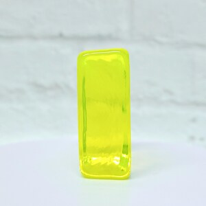 Puede incluir: Un objeto rectangular de vidrio amarillo ne&oacute;n. El objeto es de un color s&oacute;lido y vibrante y tiene bordes redondeados. El vidrio parece ligeramente texturizado, con sutiles variaciones en la superficie. El objeto est&aacute; sobre un fondo blanco.