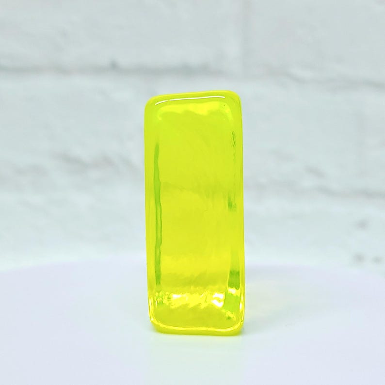 Puede incluir: Un objeto rectangular de vidrio amarillo ne&oacute;n. El objeto es de un color s&oacute;lido y vibrante y tiene bordes redondeados. El vidrio parece ligeramente texturizado, con sutiles variaciones en la superficie. El objeto est&aacute; sobre un fondo blanco.