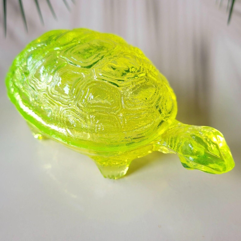 May include: A bright yellow glass turtle figurine. The turtle has a detailed shell and four legs.