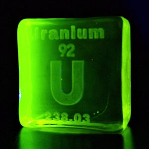 Op de afbeelding: Een heldergroene uraniumkubus met de tekst "Uranium", het nummer "92", de letter "U" en het getal "238.03". De kubus licht op tegen een donkere achtergrond.